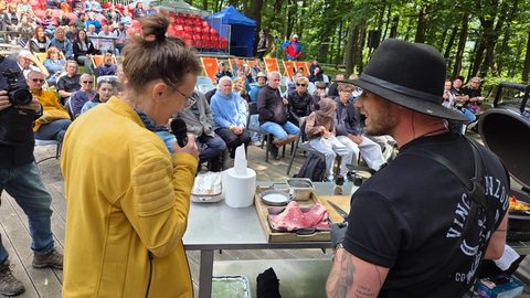 Pavla Pavelková ve&nbsp;žluté bundě moderuje s&nbsp;mikrofonem u&nbsp;kuchařského stolu, v&nbsp;hledišti v&nbsp;lese je plno