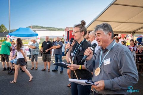 Pavla Pavelková a&nbsp;spolumoderátor s&nbsp;mikrofony a&nbsp;dřevěnými medailemi moderují před festivalovými stany